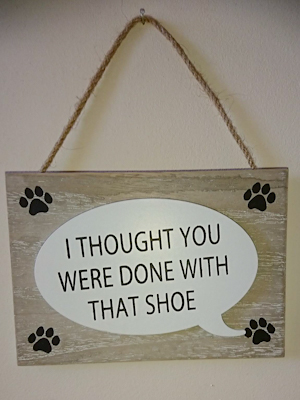 A rectangular white wash style MDF sign with a speech bubble with the quote "I thought you were done with that shoe". There is an illustrated paw print in each corner.